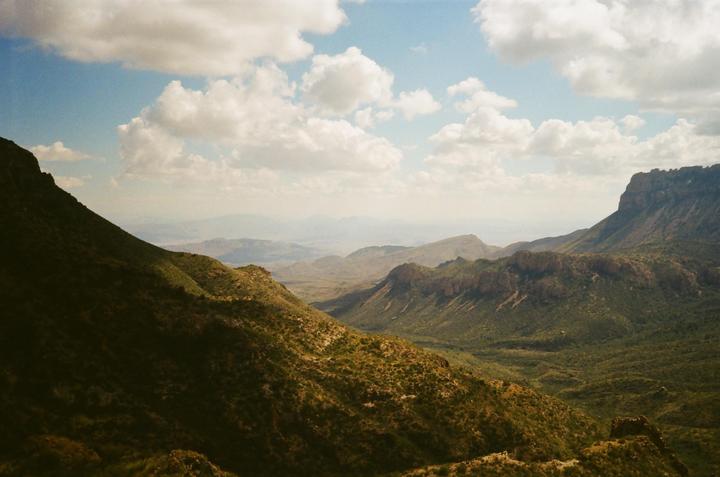 A vast mountain landscape with a valley and cloudy sky is visible.