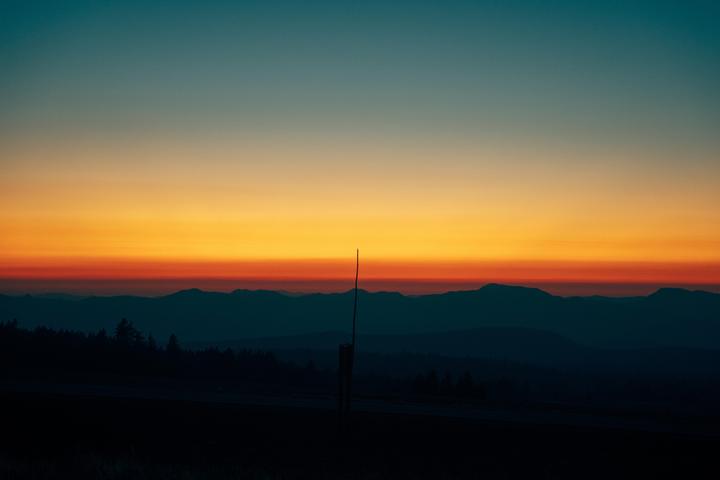 A single pole stands in front of a mountain range at sunset.