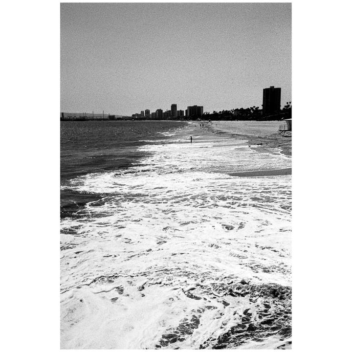 Waves crash on a beach with a city skyline in the distance.