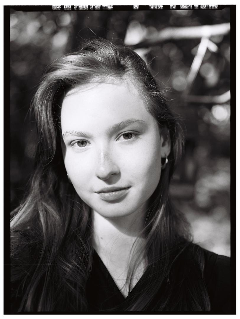 A young woman with long hair looks directly at the viewer in a black and white portrait.