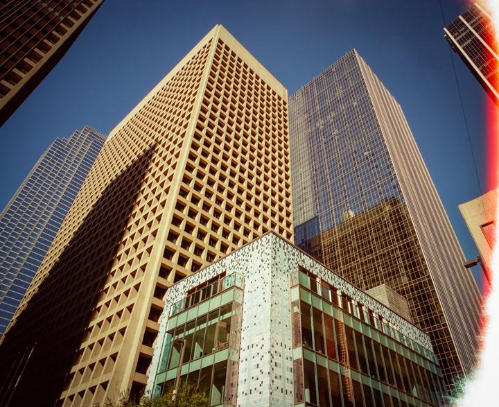 Several tall buildings with varied architectural styles rise towards a clear blue sky.