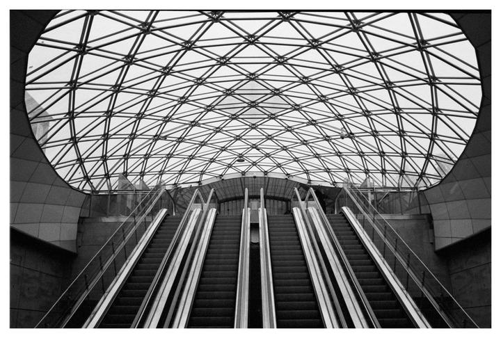 Four escalators lead up to a glass dome with a geometric metal frame.