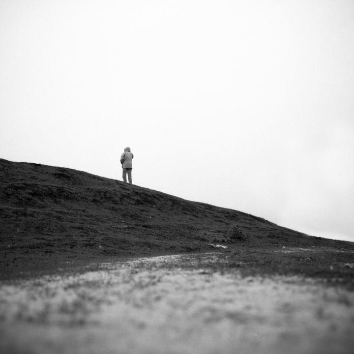 A person stands on a grassy hill under a bright, overcast sky.
