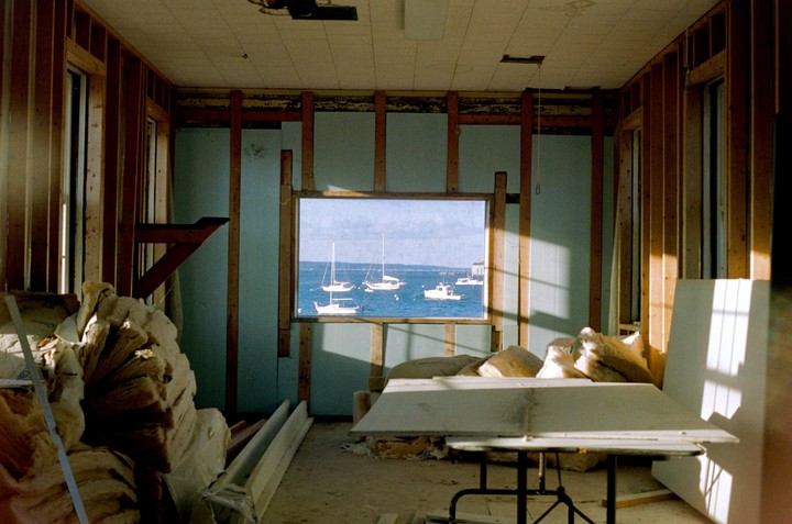 A room under construction with exposed wooden studs and insulation looks out onto a body of water with several boats.