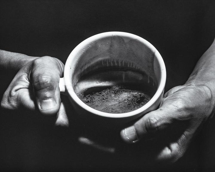 A person's hands hold a mug of coffee, with the surface of the coffee showing a distinct pattern.