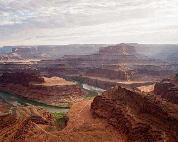 A wide river winds through a vast canyon landscape under a cloudy sky.