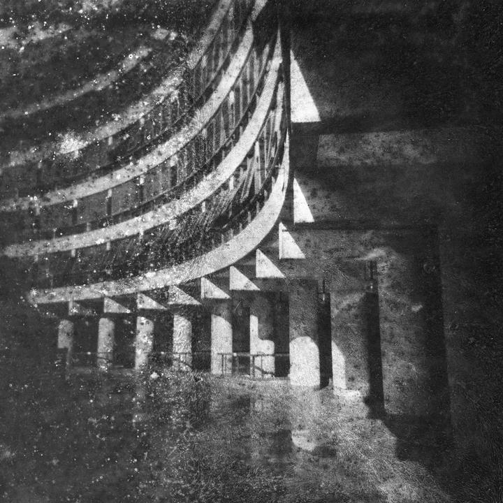 A curved building with multiple balconies and columns is shown with strong shadows and a textured, moldy appearance.