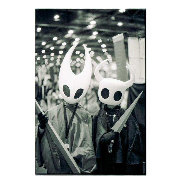 Two people in costumes with large white masks and capes stand together.