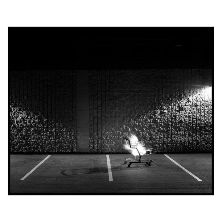 A shopping cart is on fire in a parking lot at night.