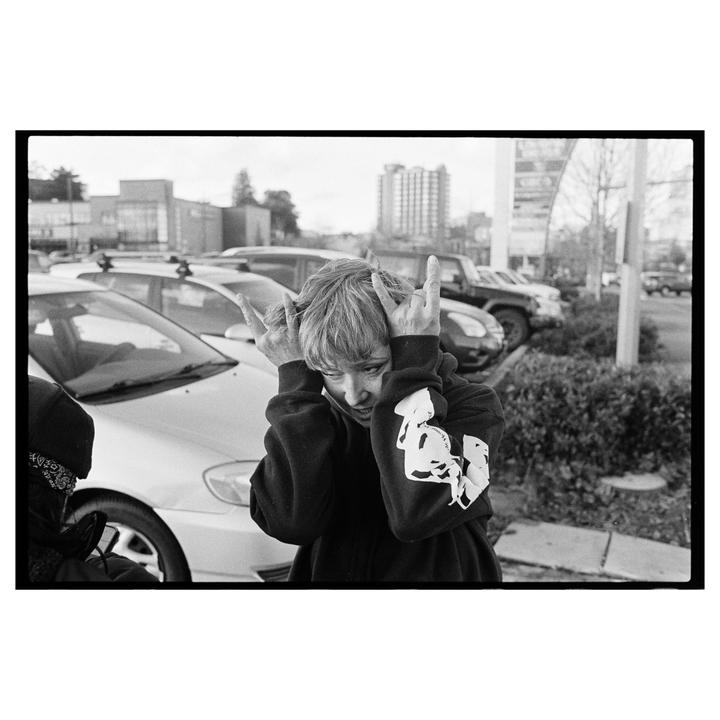 A person with short hair makes a hand gesture in a parking lot.