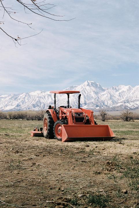 A red tractor sits in a field with snow-capped mountains in the background.