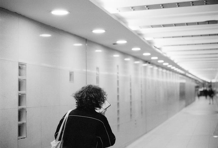 A person with curly hair and a tote bag walks away down a brightly lit hallway.