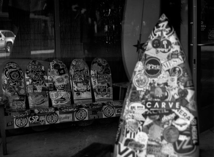 A collection of sticker-covered skateboards and a surfboard are displayed in a storefront.