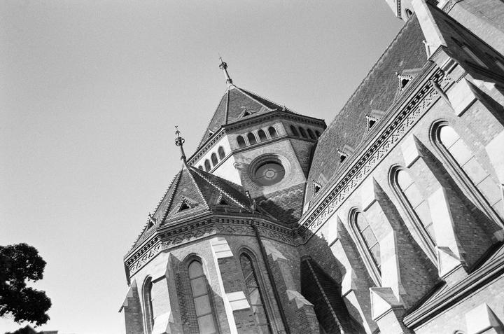 A low-angle view shows the intricate architecture of a large brick building with a prominent tower and multiple windows.