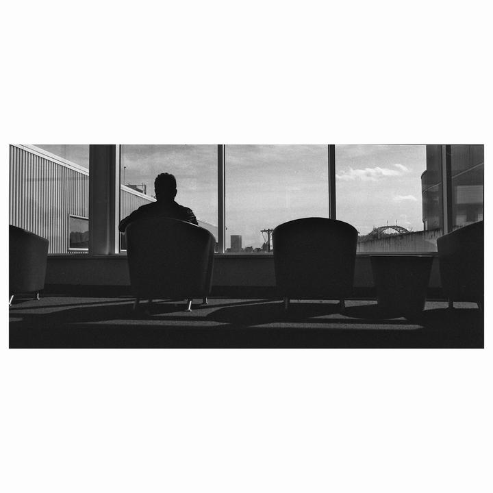 A man sits in a chair looking out a large window at a city skyline.