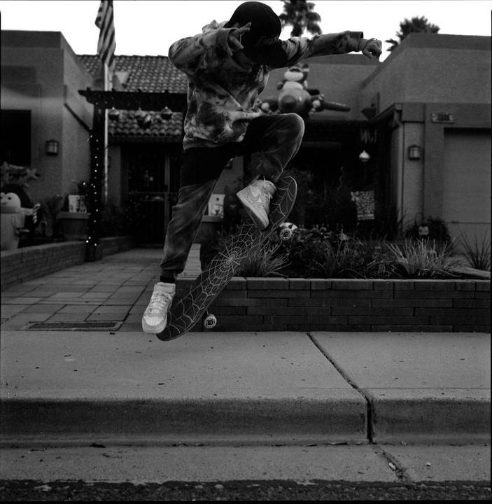 A boy on a skateboard is captured mid-air performing an ollie trick on a residential street.