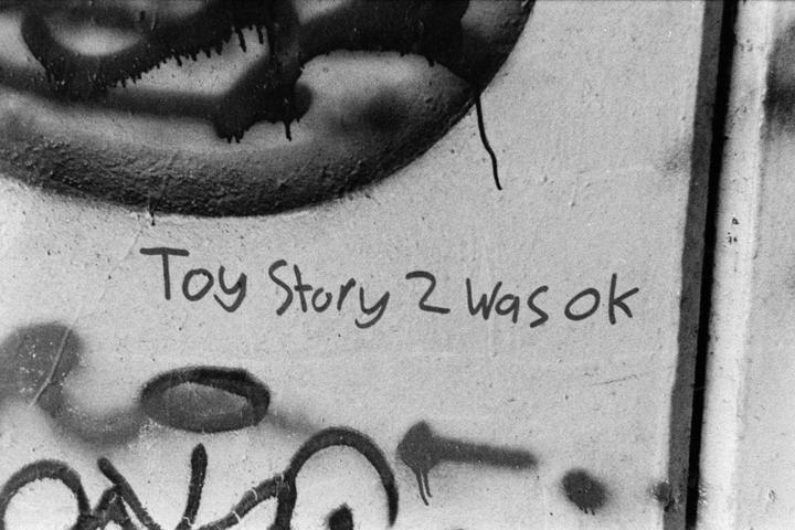 The phrase "Toy Story 2 was ok" is written on a wall with graffiti.