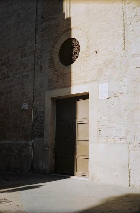 Sunlight casts a shadow across a building facade with a round window and an open door.