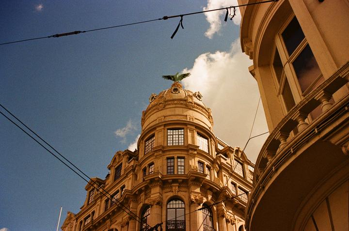 A low-angle view shows a domed building with an eagle sculpture on top, with power lines crossing the blue sky.