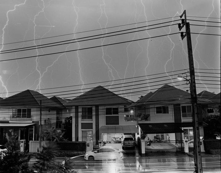 Lightning strikes illuminate the sky above houses and power lines during a thunderstorm.