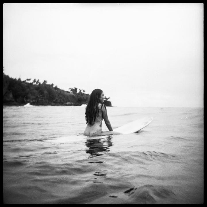 A woman sits on a surfboard in the ocean with an island in the background.