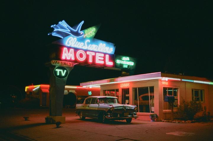 A vintage car is parked in front of the Blue Swallow Motel sign at night.