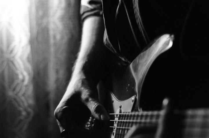 A man's hand is playing an electric guitar in a dimly lit room.