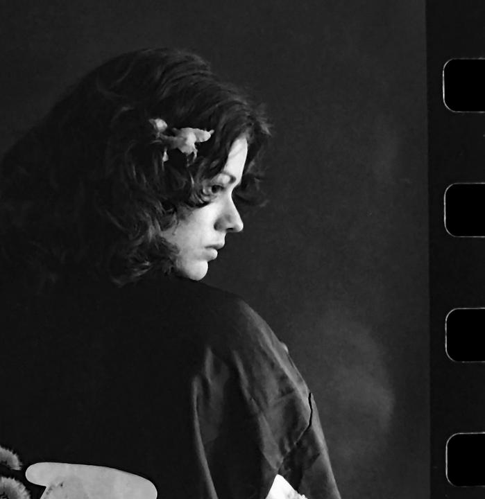 A woman with a flower in her hair looks over her shoulder, with a film strip visible on the right.