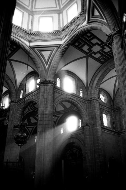 Sunlight streams through a window into a large, ornate church interior with high arched ceilings and columns.