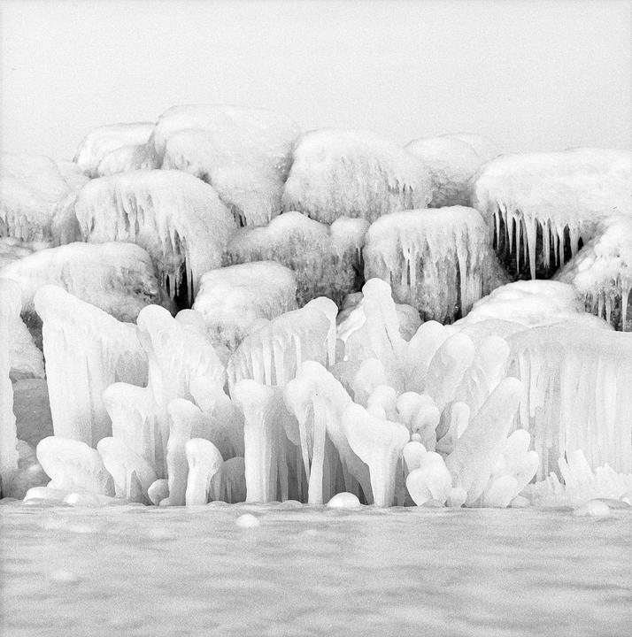A wall of ice formations and icicles covers rocks and the ground.