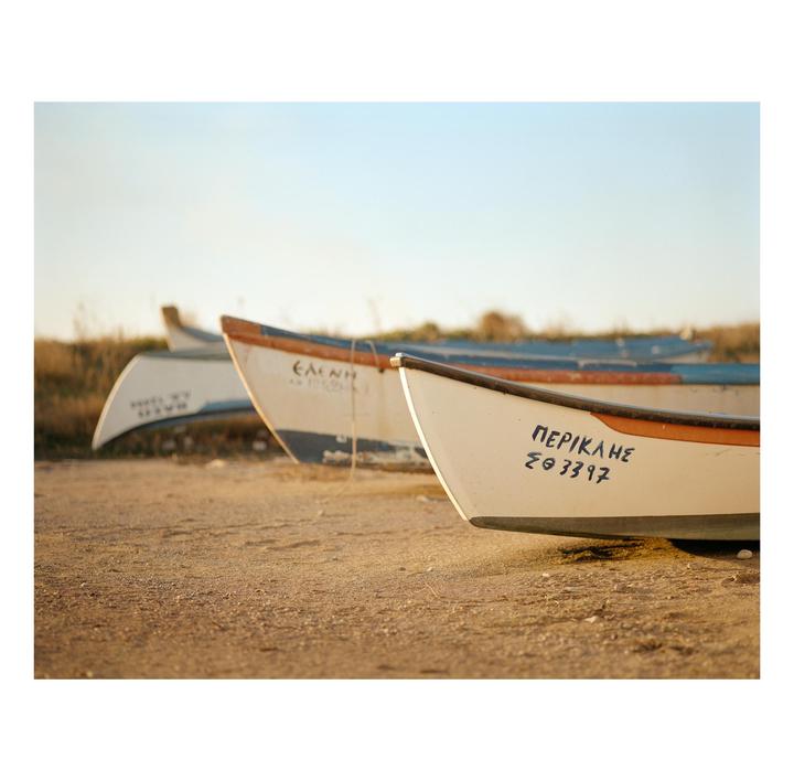 Three small boats are lined up on a sandy beach under a clear sky.