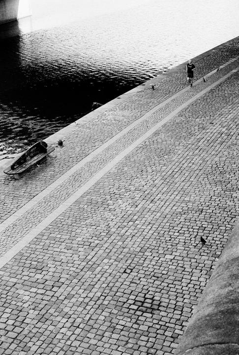A person runs along a cobblestone path next to a body of water.