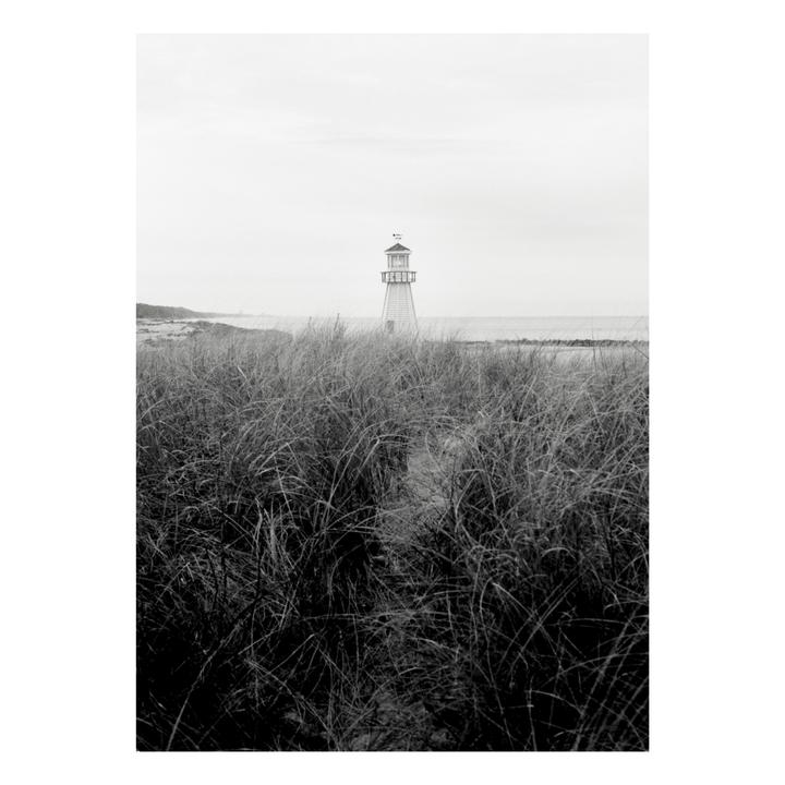 A white lighthouse stands behind tall grass on a hazy day.