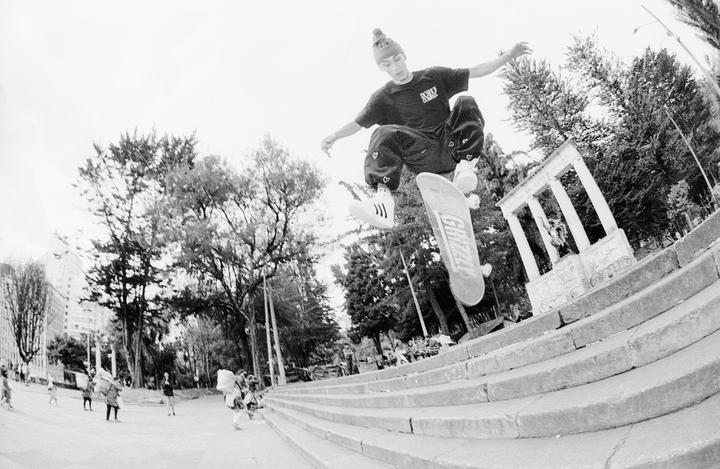 A young man on a skateboard is captured mid-air above a set of concrete steps in a park.