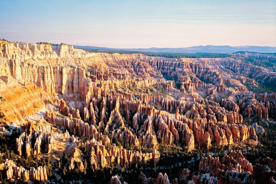 An aerial landscape view shows the vast, intricate rock formations of Bryce Canyon National Park under a clear sky.
