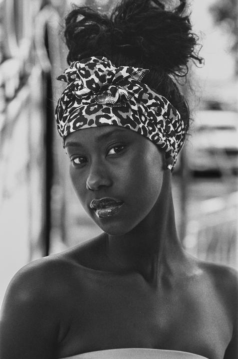 A woman with a leopard print headscarf looks directly at the viewer.