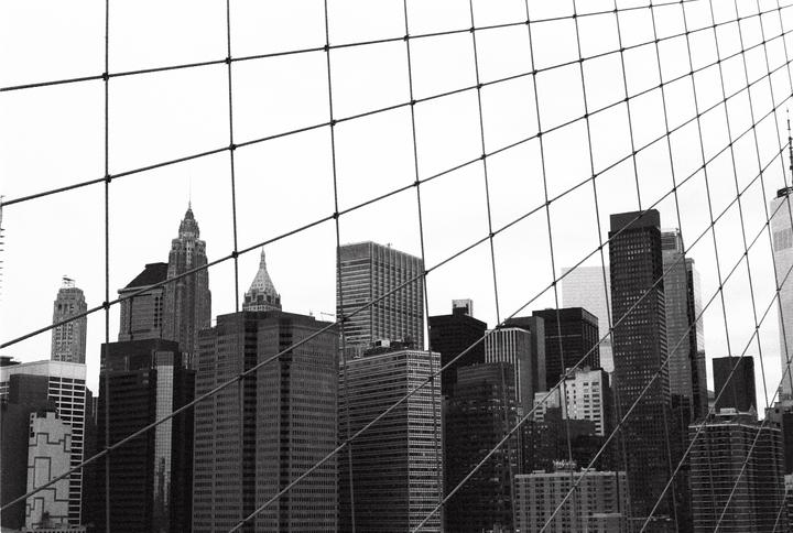 A grid of wires from the Brooklyn Bridge frames a view of the New York City skyline.