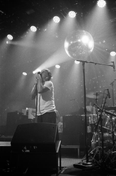 A man sings into a microphone on a stage with a disco ball and stage lights.