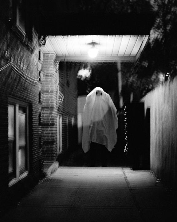 A person dressed as a ghost floats under an awning at night.