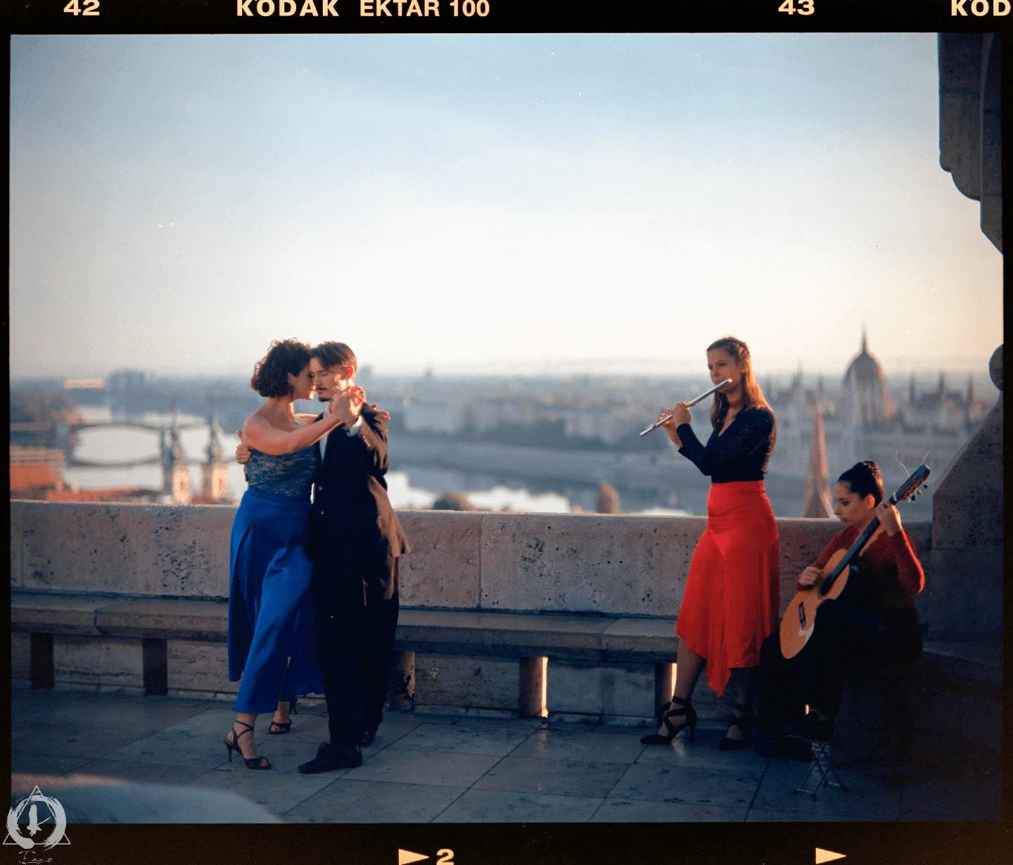 A couple dances on a rooftop while two women play music with a flute and a guitar, overlooking a city.