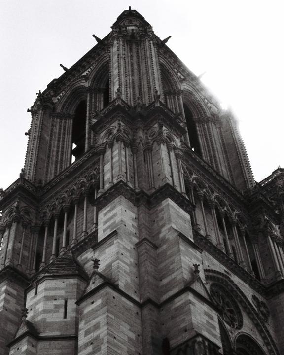 The corner of a gothic cathedral tower is seen from below, with light shining through the arches.