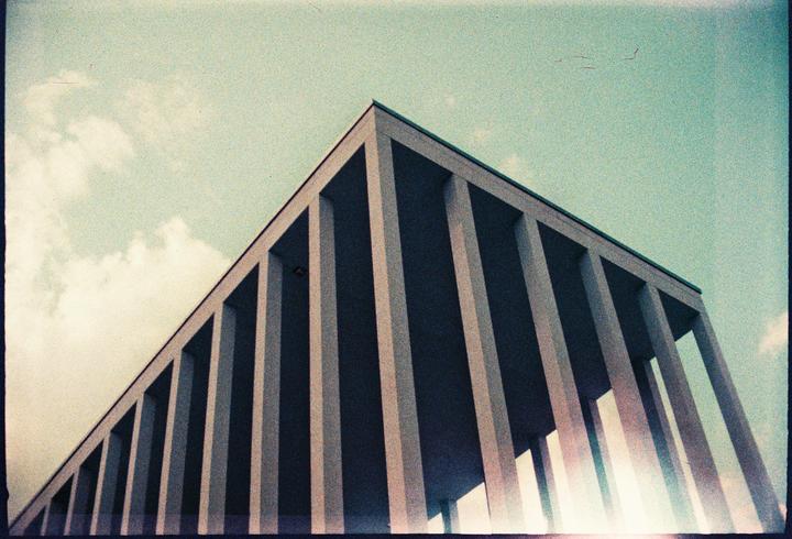 A low-angle view shows the corner of a building with many vertical columns and a bright sky.