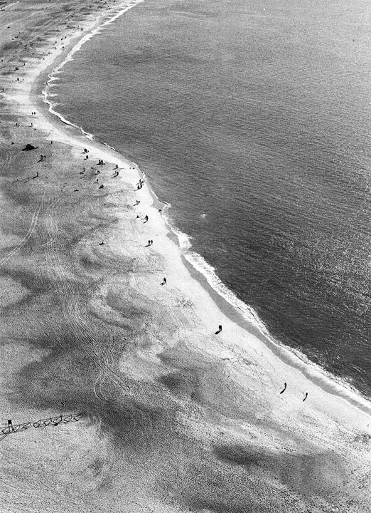 An aerial view shows a beach with people walking along the shoreline next to the ocean.