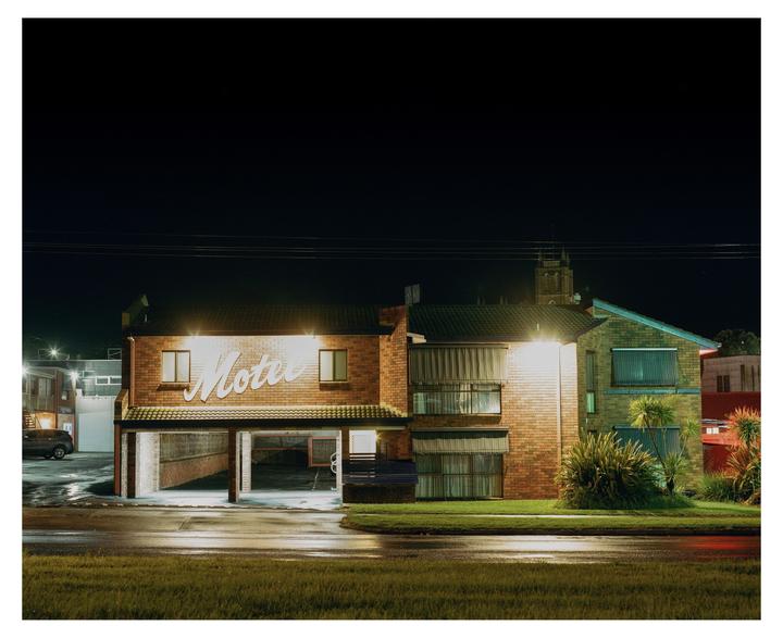 A motel with an illuminated sign is visible at night, with a wet street in the foreground.