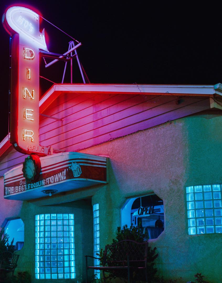 A diner with a neon sign and glowing blue windows is illuminated at night.