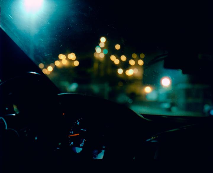 The interior of a car is visible at night, with blurred lights visible through the windshield.