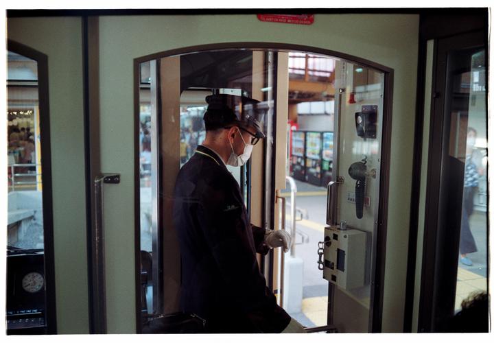 A train conductor wearing a face mask and uniform stands in the doorway of a train.