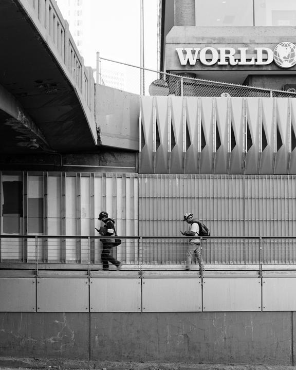 Two men walk along a raised walkway next to a building with the word "WORLD" on it.