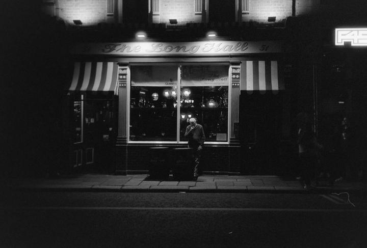 A man stands outside a pub called The Long Hall at night.