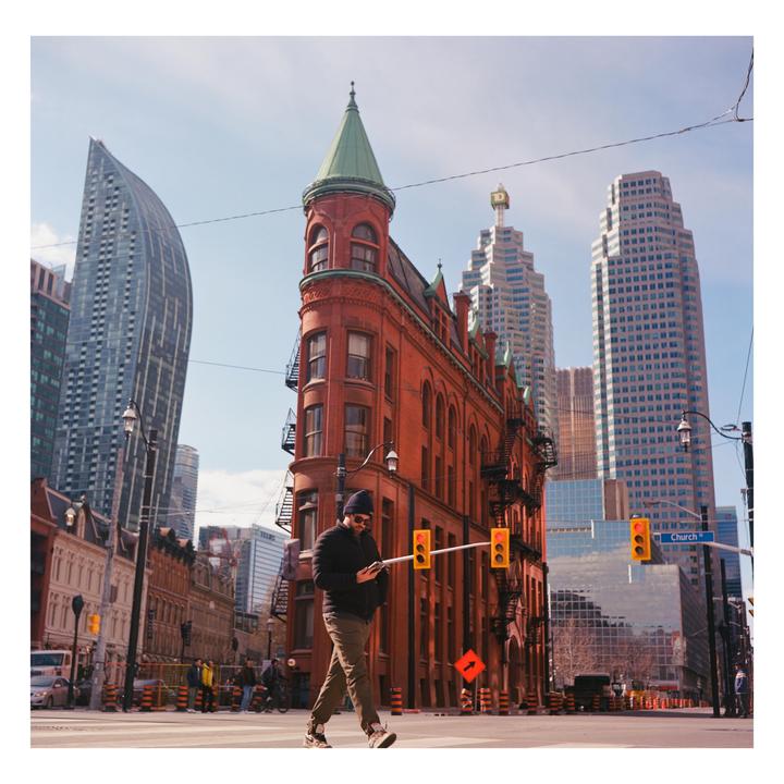 A man crosses a street in front of a red brick flatiron building with a green turret.